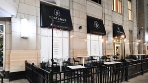 An outdoor seating area with tables and chairs, a black fence, and banners for a wine bar and bistro. - 4 Downtown Indy SkyWalk to Gainbridge Lucas Oil Conv Cntr (Indianapolis)