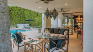 An outdoor patio with a pool, seating area, and a glass wall with a view of the greenery.