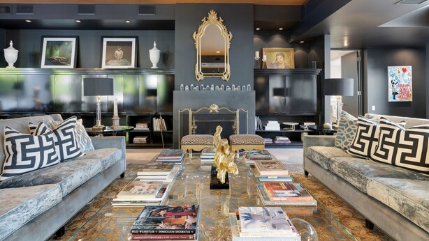A modern living room with a marble coffee table, two sofas with patterned cushions, a gold-framed mirror, and a fireplace.