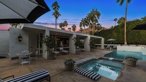 A modern outdoor pool area with lounge chairs, a dining setup, and a covered patio.
