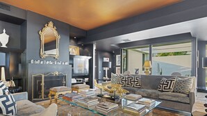 A modern living room with a dark color scheme, a glass coffee table, and a sofa with patterned cushions.