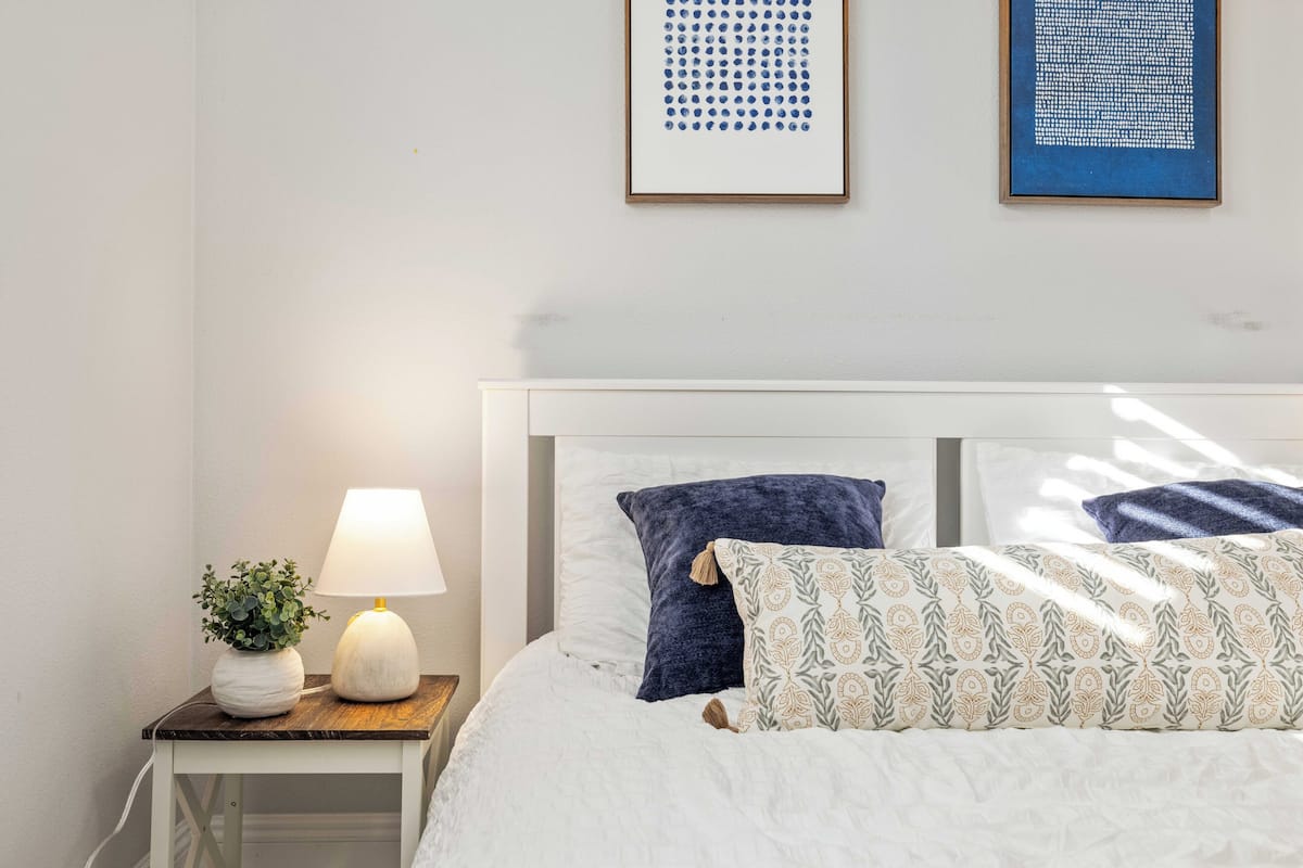 A neatly made bed with patterned pillows, a bedside lamp, and a small plant on a nightstand.