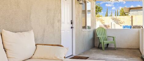 A covered porch with a beige sofa, a green chair, and a white door.