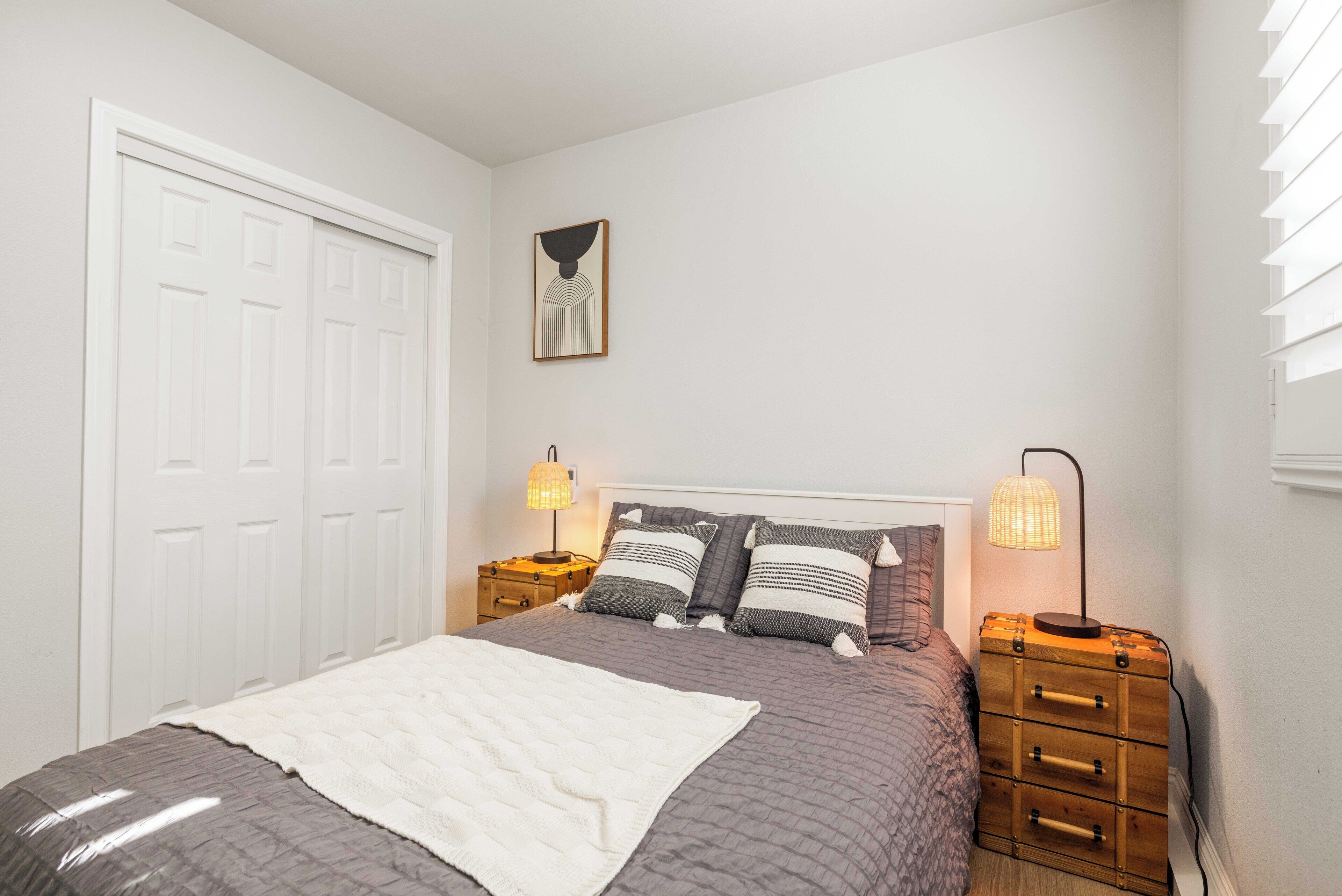 A bedroom with a bed, two bedside tables, a dresser, a door, and a wall-mounted artwork.