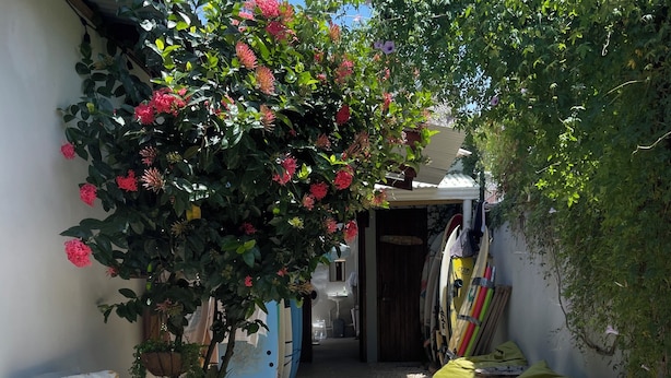 Un étroit sentier extérieur, agrémenté d’un petit espace de repos, d’un endroit pour ranger les planches de surf et de diverses plantes en pot.