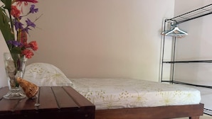 Un lit recouvert d’une couvre-lit à motifs floraux, une table de chevet ornée d’un vase de fleurs et un porte-vêtements en métal.