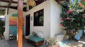 Un espace extérieur abrité, aménagé avec un banc en bois, une petite table et un pot de fleurs.