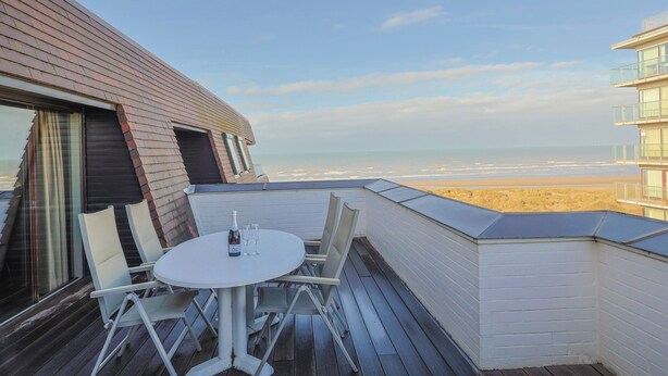 Eine Dachterrasse mit rundem Tisch und Stühlen mit Blick auf einen Strand.