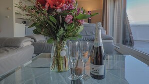 Ein Glastisch mit einer Champagnerflasche, zwei Gläsern und einem Blumenstrauß in einem modernen Zimmer mit Blick.