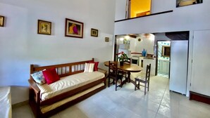 A living room with a sofa, dining table, chairs, and a kitchen area with a refrigerator and microwave.