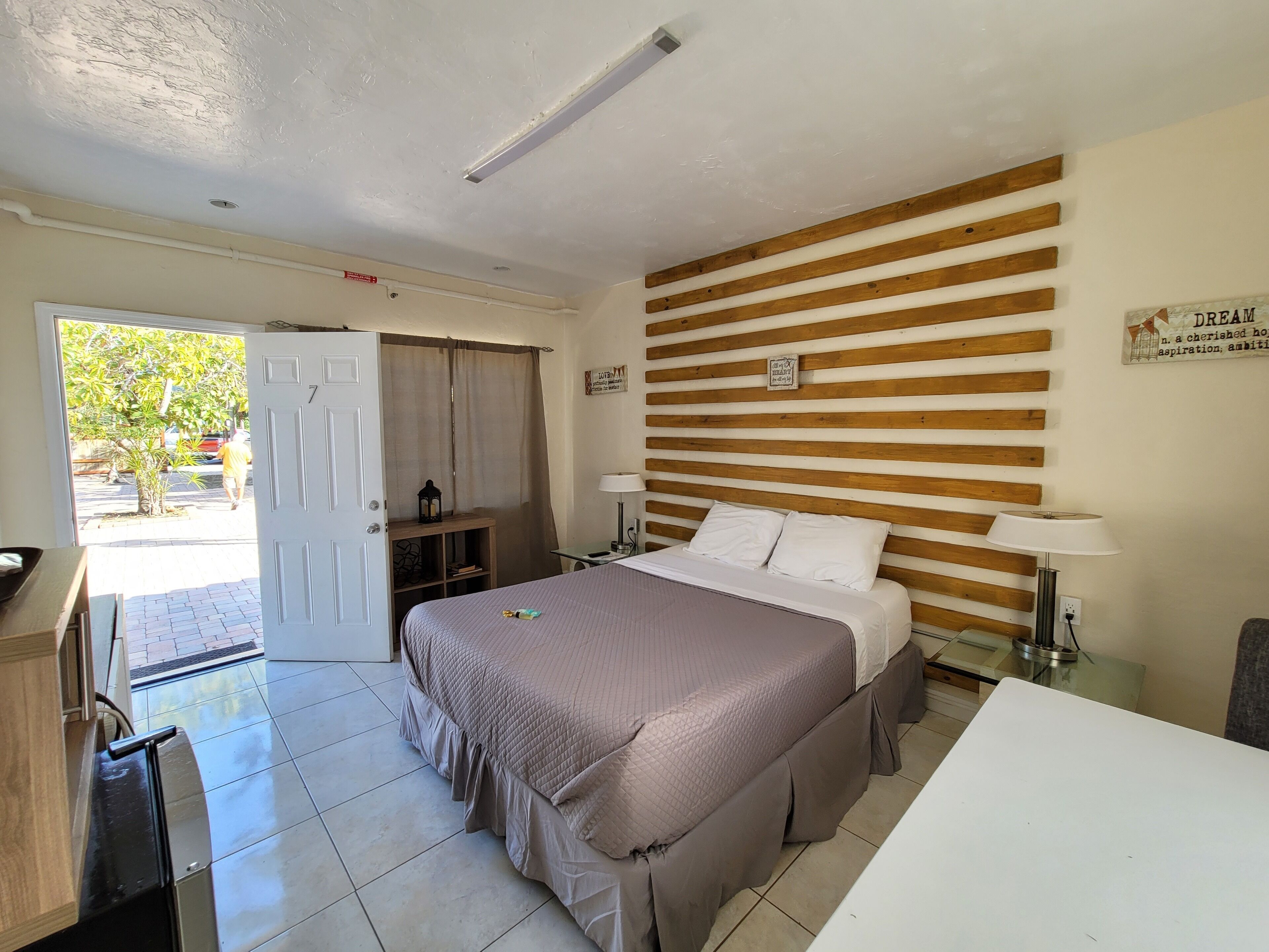 Ein Hotelzimmer mit einem Bett, Nachttischen, einem Schreibtisch und einer Tür, die auf einen Balkon führt.