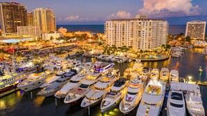 A marina with multiple yachts docked, surrounded by high-rise buildings and a cityscape.
