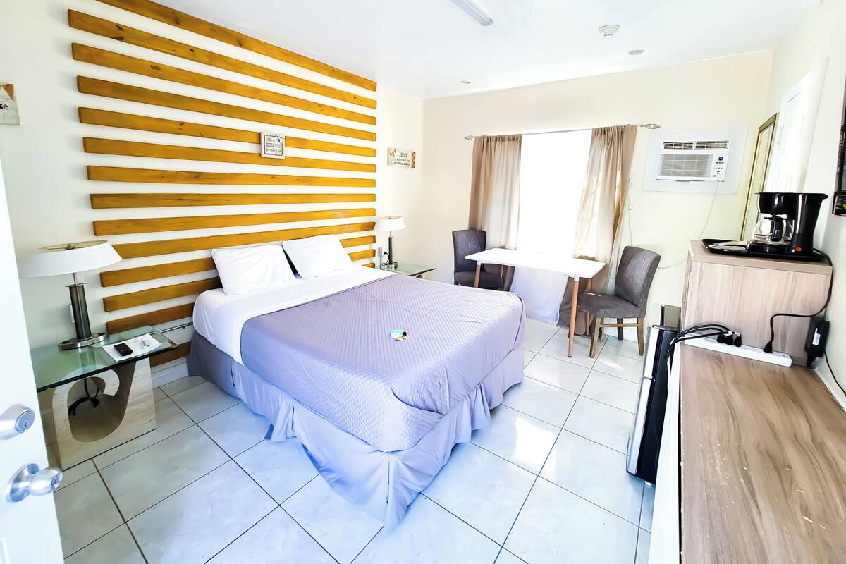 A hotel room with a bed, a desk, a chair, a coffee maker, and a window with curtains.