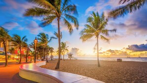 A beach with palm trees, a lifeguard tower, and a curved walkway.