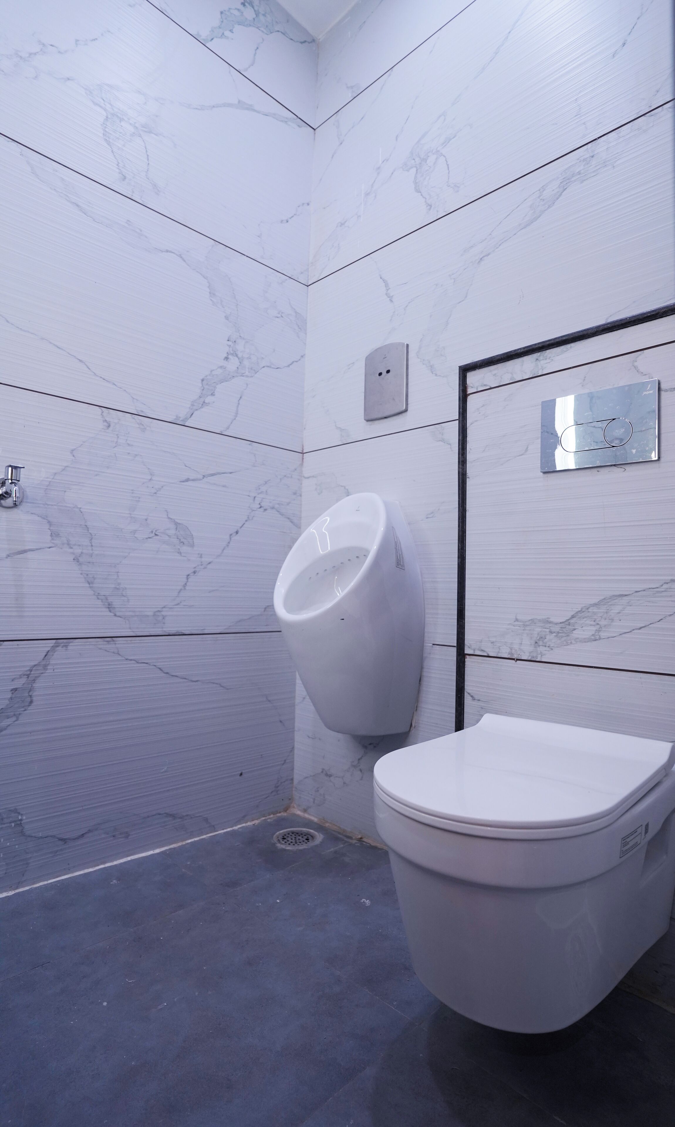 Une salle de bain moderne avec un mur en marbre, un urinoir et des toilettes.