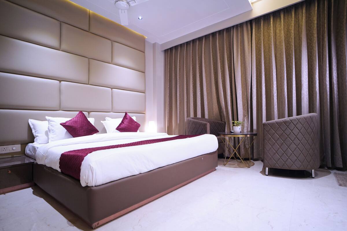 Ein modernes Hotelzimmer mit einem großen Bett, einem kleinen Beistelltisch, einem Sessel und einem großen Fenster mit Vorhängen.