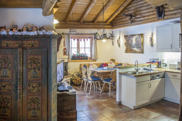 A cozy kitchen with a wooden ceiling, a dining area with blue chairs, and a small island with a sink.