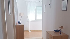 A hallway with a wooden cabinet, a desk with a lamp, and a window with curtains. - PAP'S HOUSE  (Rodes)