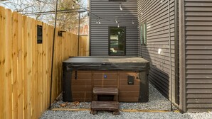 Una vasca idromassaggio in un giardino privato con una recinzione in legno, un pontile di legno e una casa con rivestimento.