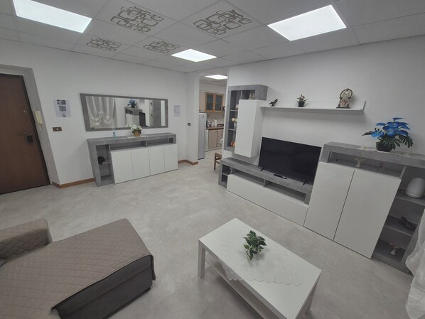 A modern living room with a sofa, a coffee table, a TV, and a kitchen area in the background.