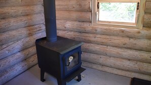 A wood-burning stove in a log cabin room with a window.