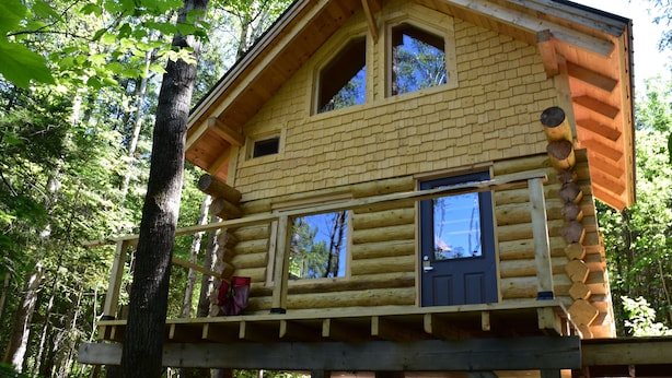 A log cabin with a balcony, surrounded by trees.