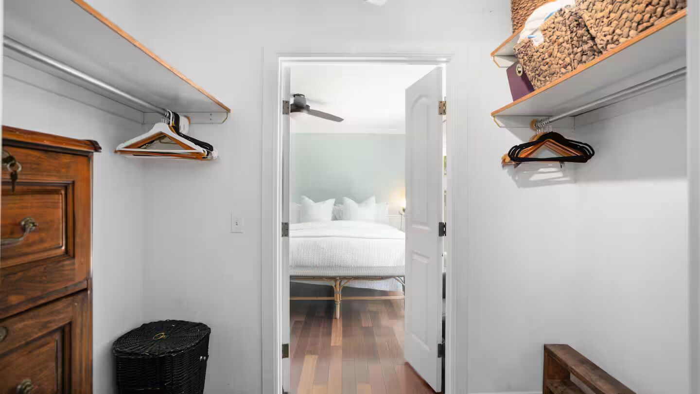 A narrow hallway with a bed at the end, wooden furniture, and hanging clothes racks.