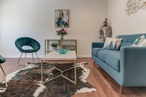 A living room with a blue sofa, a teal chair, a white coffee table, and a cowhide rug. - @ Marbella Lane - Boho 'n Sleek Rtreat Pool Tble (Union City)