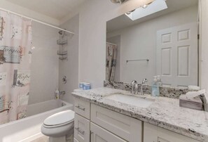 A bathroom with a white toilet, a sink with a marble countertop, a shower with a shower curtain, and a mirror above the sink. - @ Marbella Lane - Boho 'n Sleek Rtreat Pool Tble (Union City)