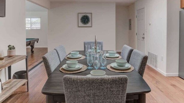 A dining room with a rectangular table set for six, surrounded by grey upholstered chairs.