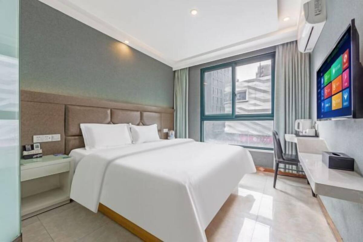 A hotel room with a bed, bedside table, and a window with a city view.