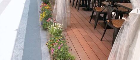 Ein Außenbereich mit Tischen und Stühlen, einer Holzterrasse und einem Blumenbeet am Rand.