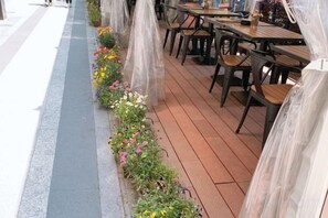 Un espace extérieur aménagé avec des tables et des chaises, une terrasse en bois et un parterre de fleurs le long du bord.