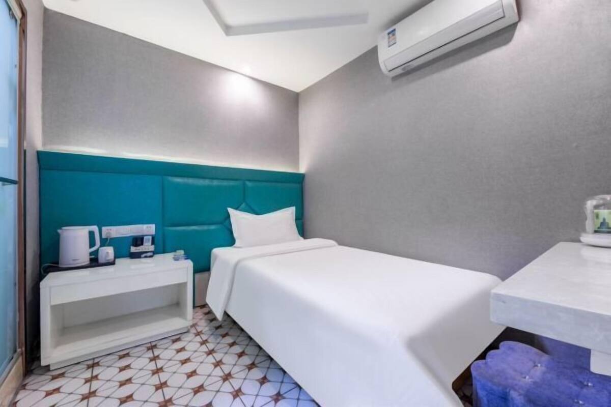 A hotel room with a teal headboard, a white bed, a small bedside table with a lamp, and a white nightstand.
