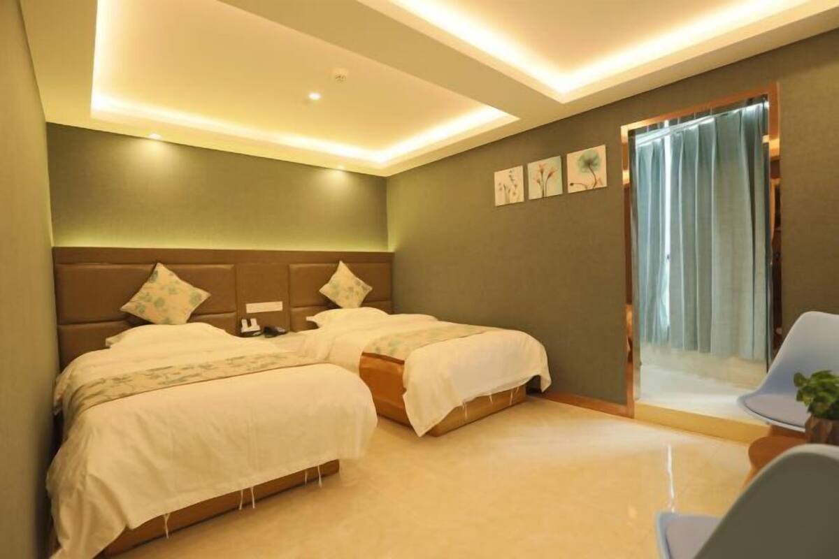 A hotel room with two beds, a small table, a chair, and a view of the outside.