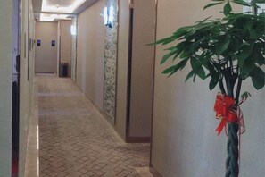 A hotel corridor with a tiled floor, a plant with a red ribbon, and a wall with a textured pattern. - Man'ai Hotel (Shanghai)