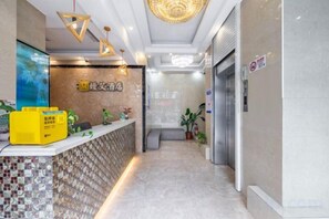 A hotel reception area with a reception desk, a wall-mounted sign, and a hallway leading to an elevator. - Man'ai Hotel (Shanghai)