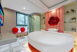 Une chambre moderne avec un grand lit, une coiffeuse avec un miroir et un coin salon avec des fauteuils rouges.