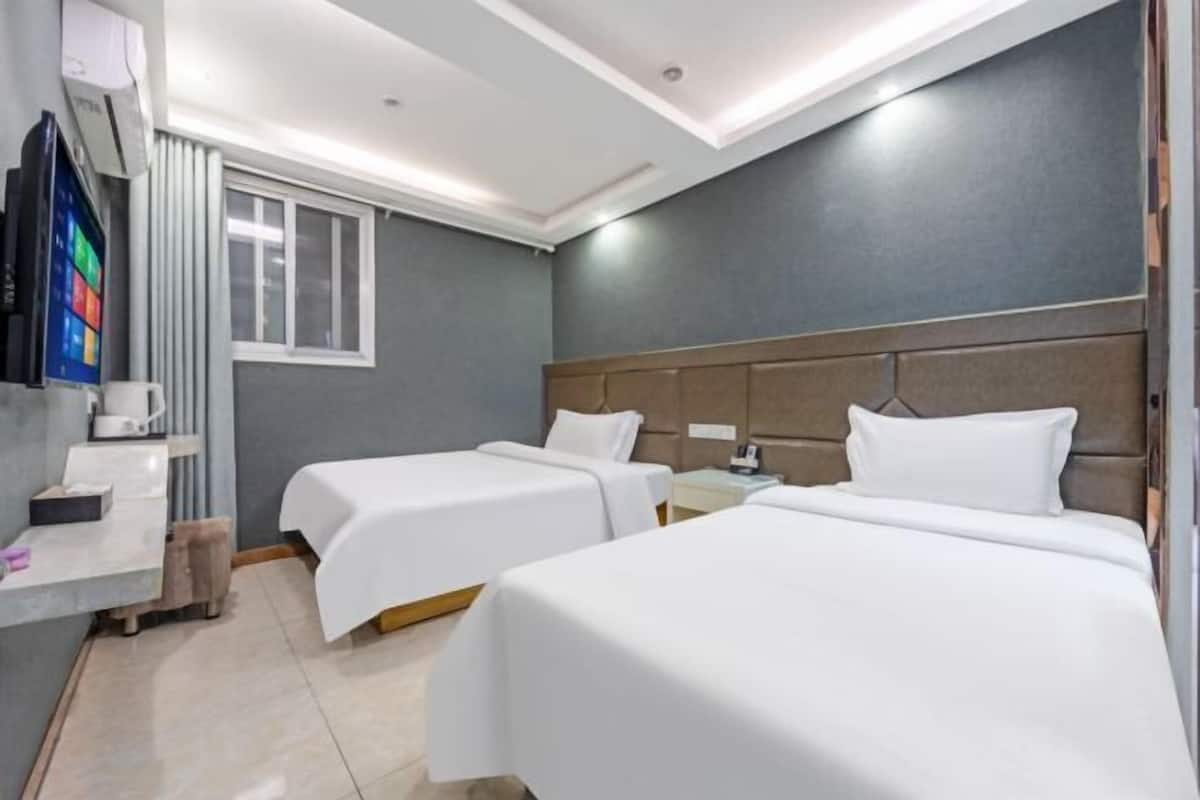 A hotel room with two single beds, a small desk with a chair, a TV, and a window.