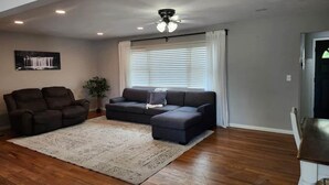 Una sala de estar con sofá, sillón, mesa de centro, alfombra y ventilador de techo.