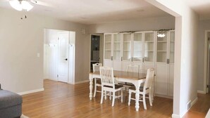 Comedor con mesa de madera y sillas blancas, ventilador de techo y armarios blancos con puertas de cristal.
