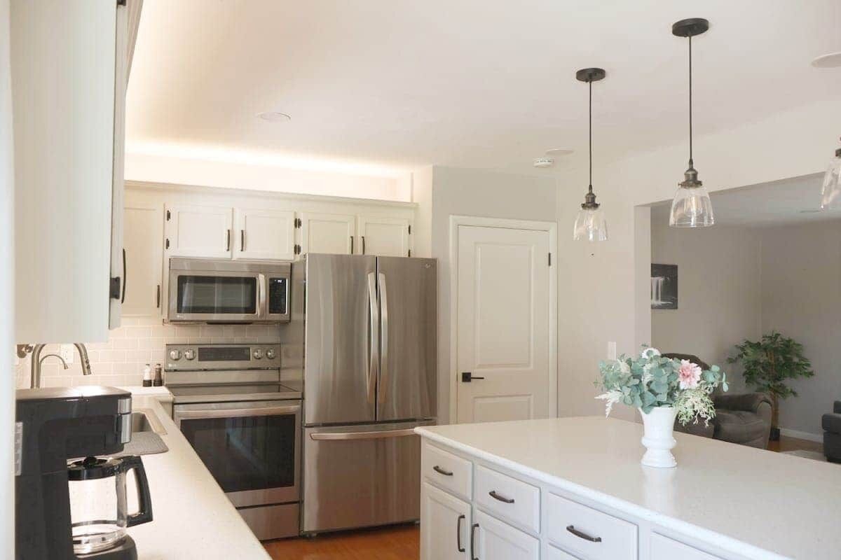 Una cocina con electrodomésticos de acero inoxidable, armarios blancos e iluminación colgante.