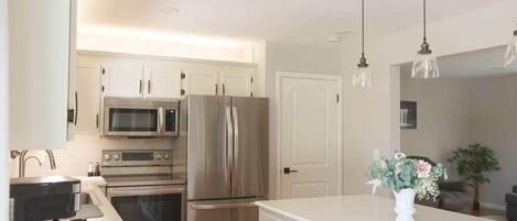 Una cocina con electrodomésticos de acero inoxidable, armarios blancos e iluminación colgante.