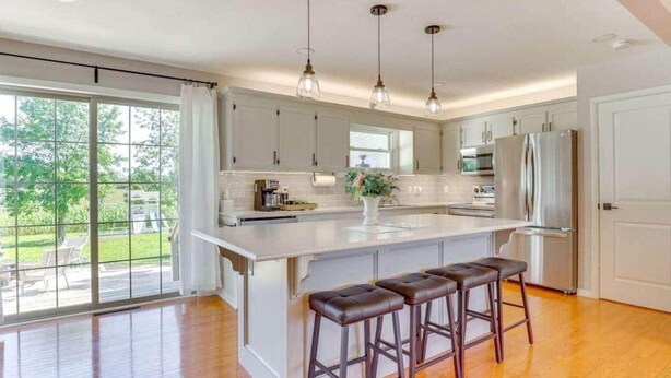 Cocina moderna con una isla grande, luces colgantes y vistas al exterior.