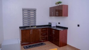 A compact kitchen with wooden cabinets, a black countertop, and a small window. - Bamgbose Apartments - Sleeps 2 - Parking - Balcony (Lagos)