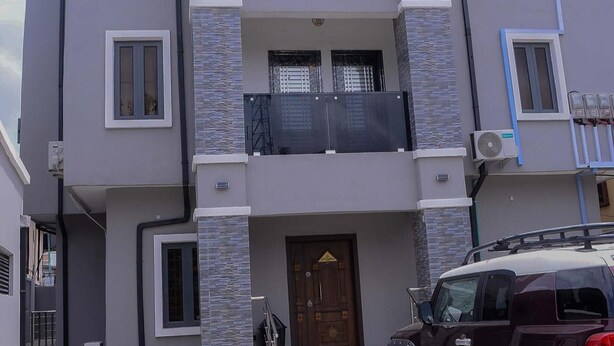A multi-story residential building with a central entrance, a balcony on the upper floor, and a parked car in front. - Bamgbose Apartments - Sleeps 2 - Parking - Balcony (Lagos)