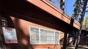 A hot tub with a wooden deck, a window with blinds, and a sign prohibiting diving.