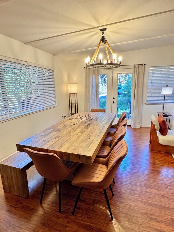 A dining room with a long wooden table, cushioned chairs, a chandelier, and large windows with blinds. - Charming 4-bedroom house in delightful South Lake Tahoe near Tahoe golf course (South Lake Tahoe)