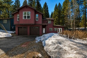 A two-story red house with a garage, surrounded by snow and trees.