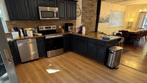 A modern kitchen with dark cabinets, stainless steel appliances, a granite countertop, and a wooden floor.